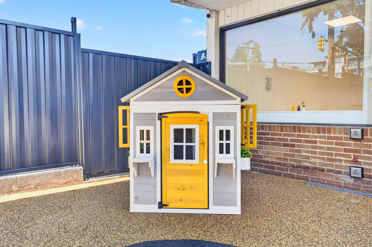 Grey playhouse with a bright yellow door in the MIM yard